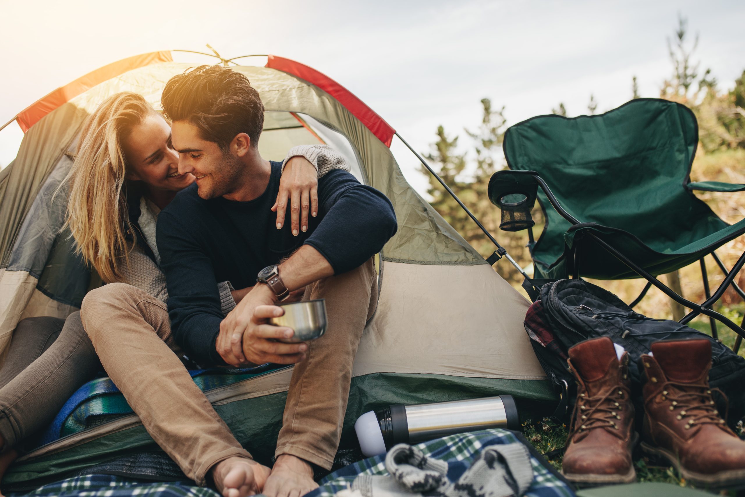 Young couple sititng inside a tent at a campsite, with a green camping chair next to them. There are plenty of fun places to camp near San Antonio Texas!