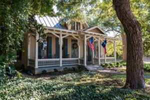 Texas house with a white front porch and black shutters shaded by a live oak tree in the King William Historic District San Antonio