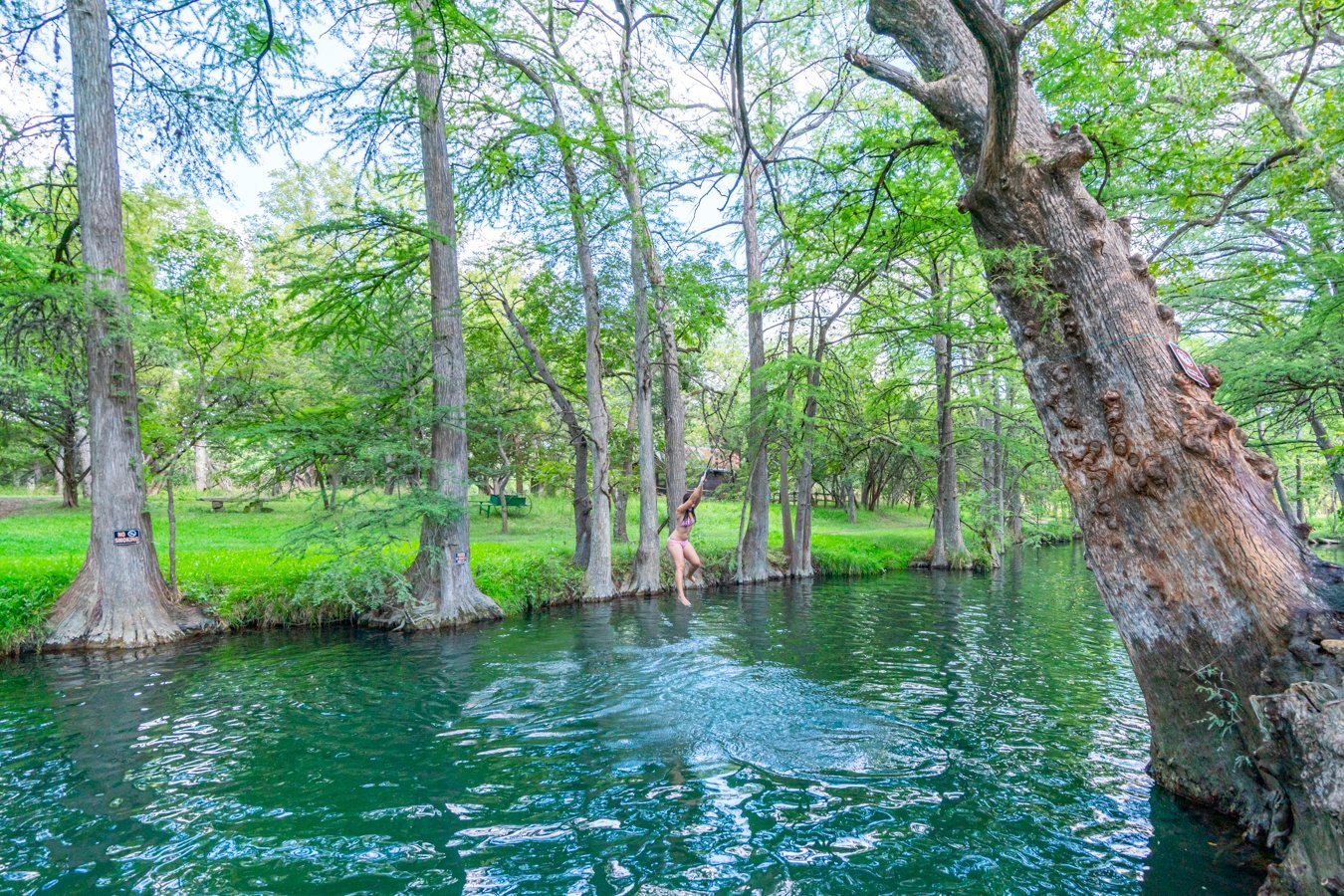 Kate Storm swinging from a metal ring above the water at the Wimberley Blue Hole