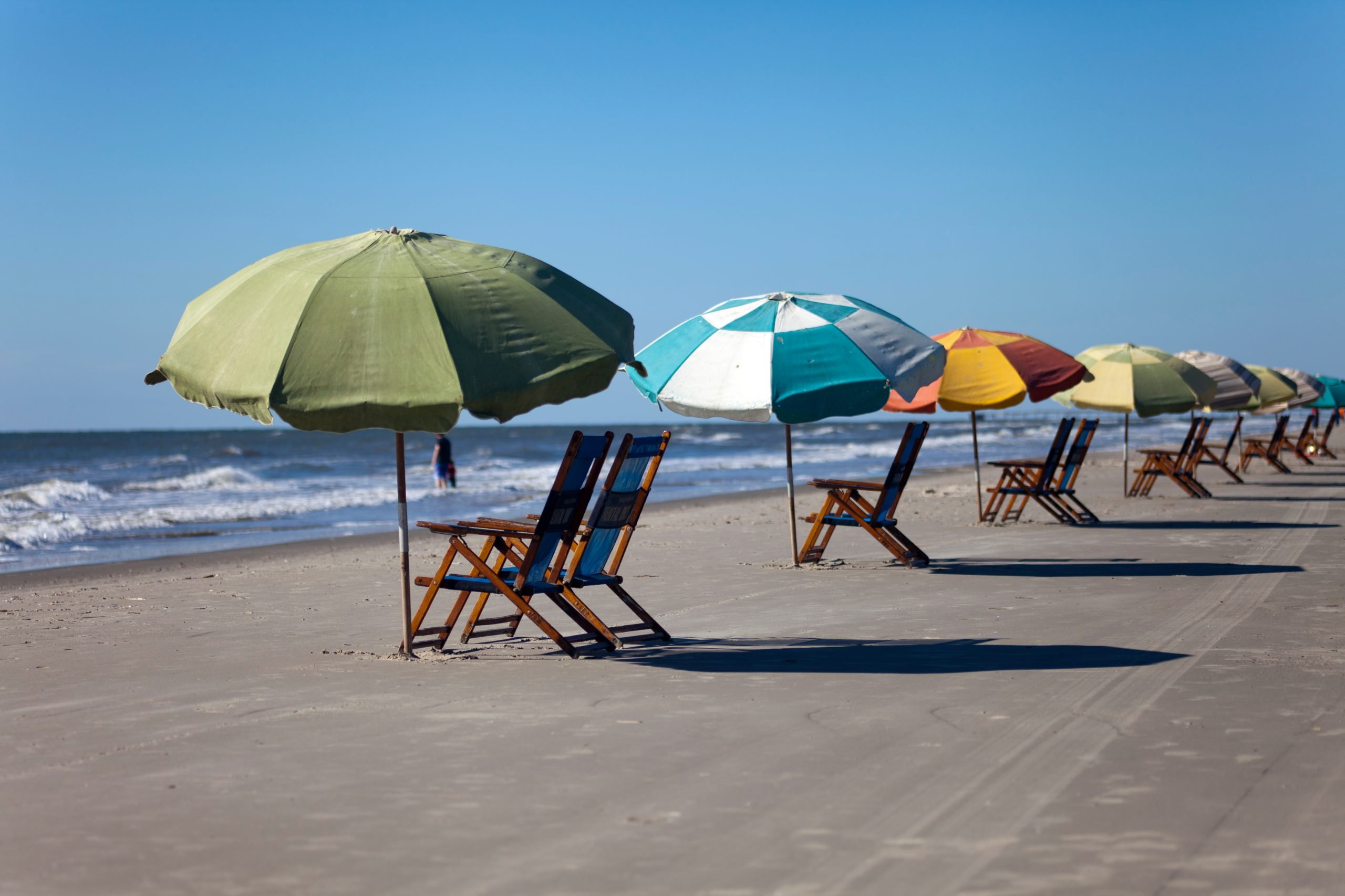 Colorful umbrellas set up on the sandy beach with chairs in Galveston, one of the best day trips from Houston TX