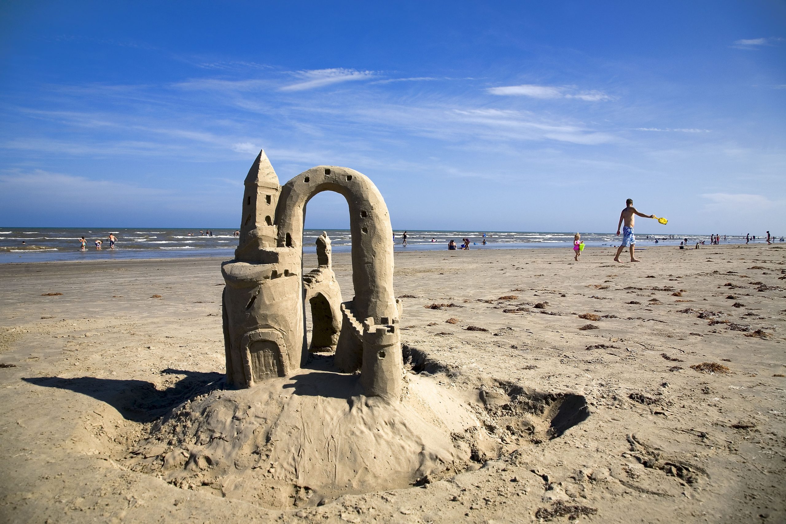 Small sandcastle on the Port Aransas beach with children playing in the background. port aransas is one of the best destinations for spring break in texas