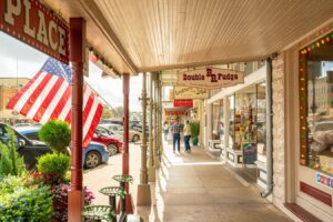 signs for shops along main street with an american flag blowing. visiting main street is one of the best things to do in fredericksburg tx