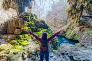 kate storm standing with her arms spread in front of westcave preserve texas waterfall