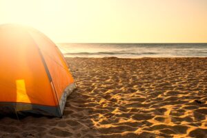 orange tent on the sand with water in the background at sunrise when beach camping texas