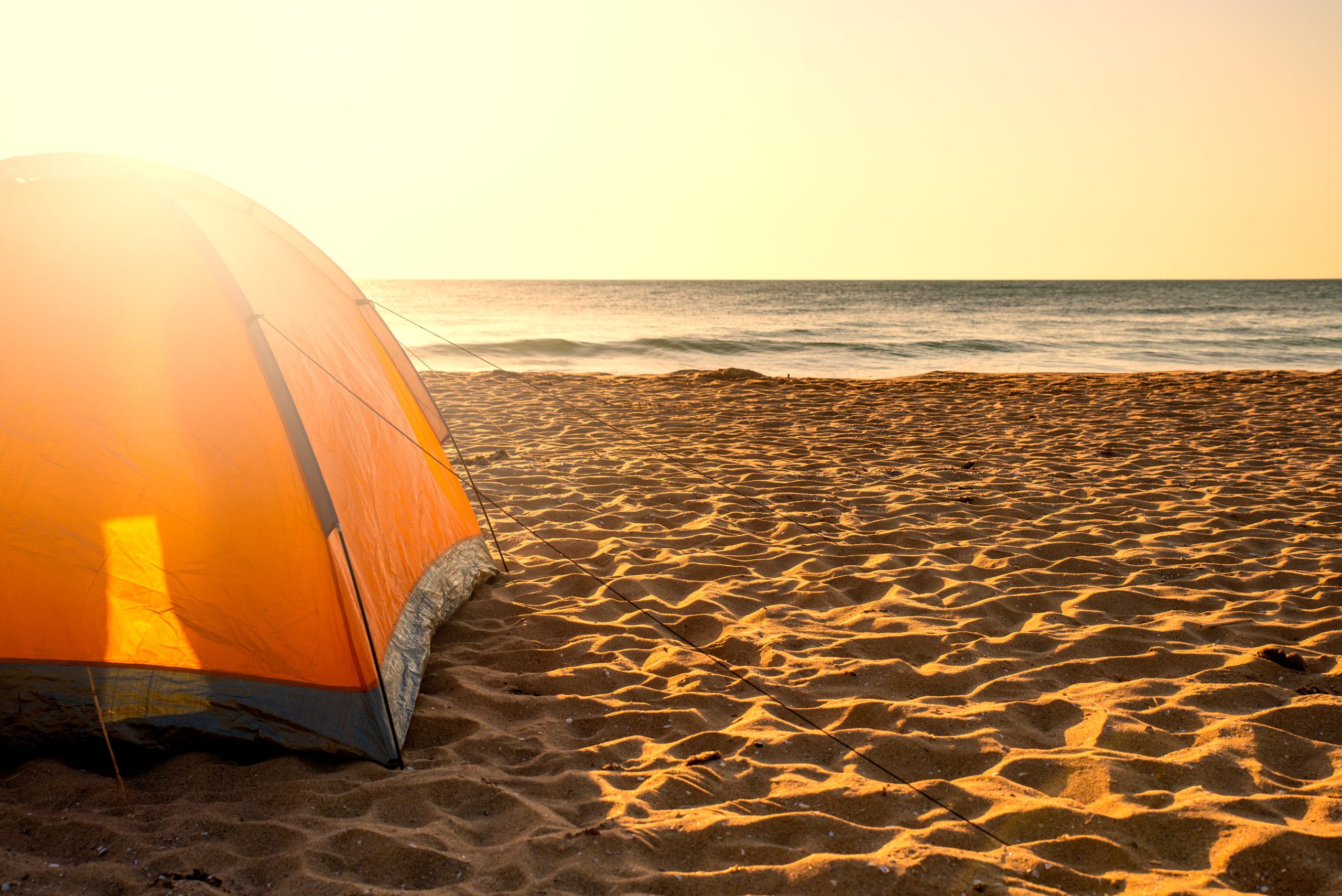 orange tent on the sand with water in the background at sunrise when beach camping texas