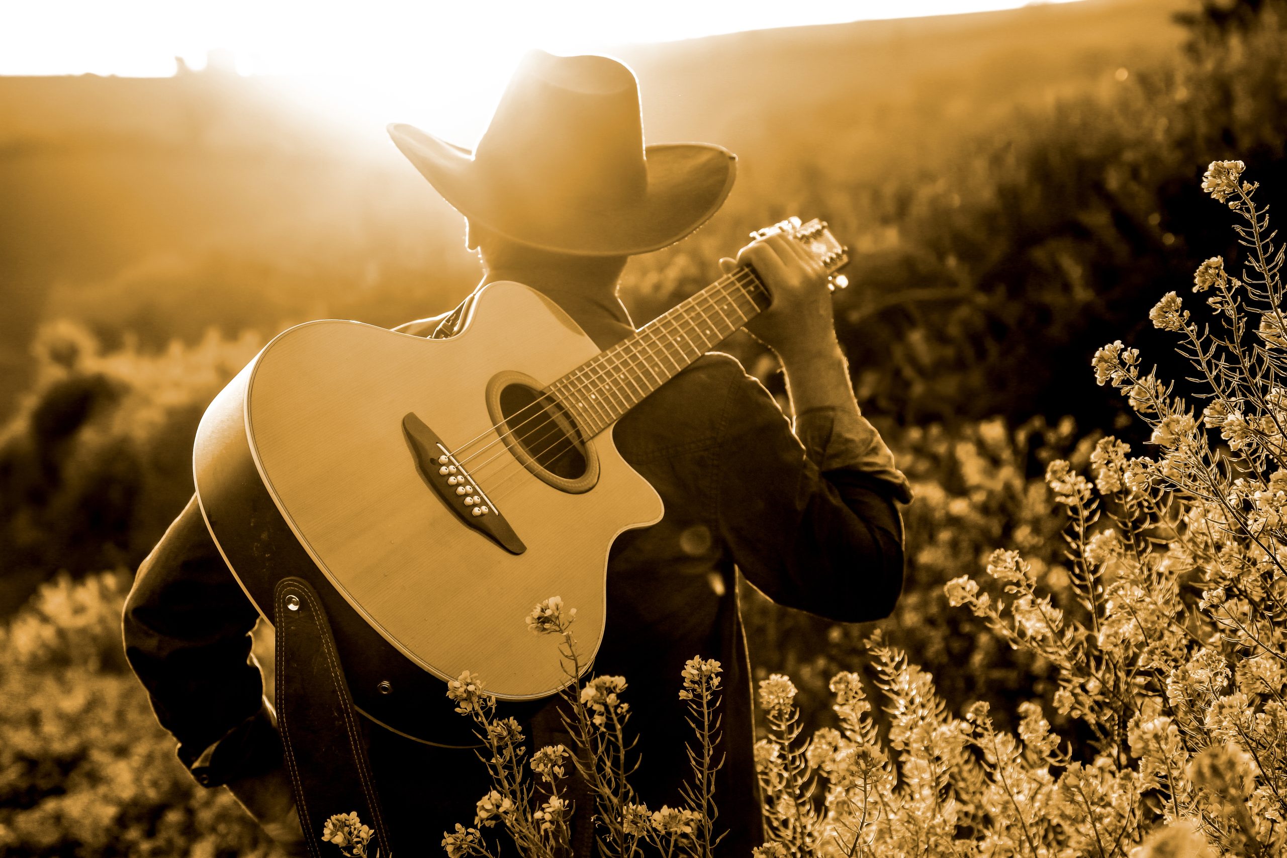 man in a cowboy hat carrying a guitar at sunset, representative of famous songs about texas